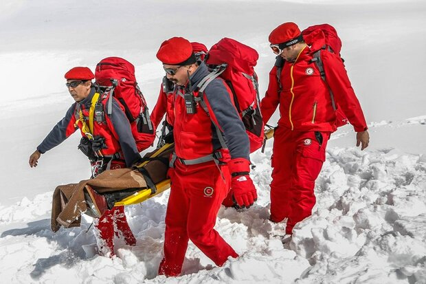 A group of rescuers in red uniforms carrying a stretcher through snowy terrain