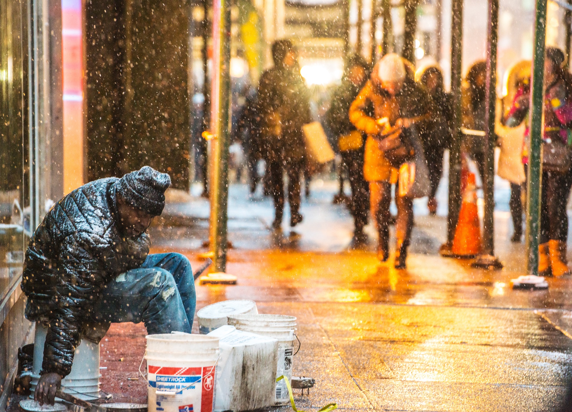 A homeless person sitting on buckets in the falling snow during Christmas time